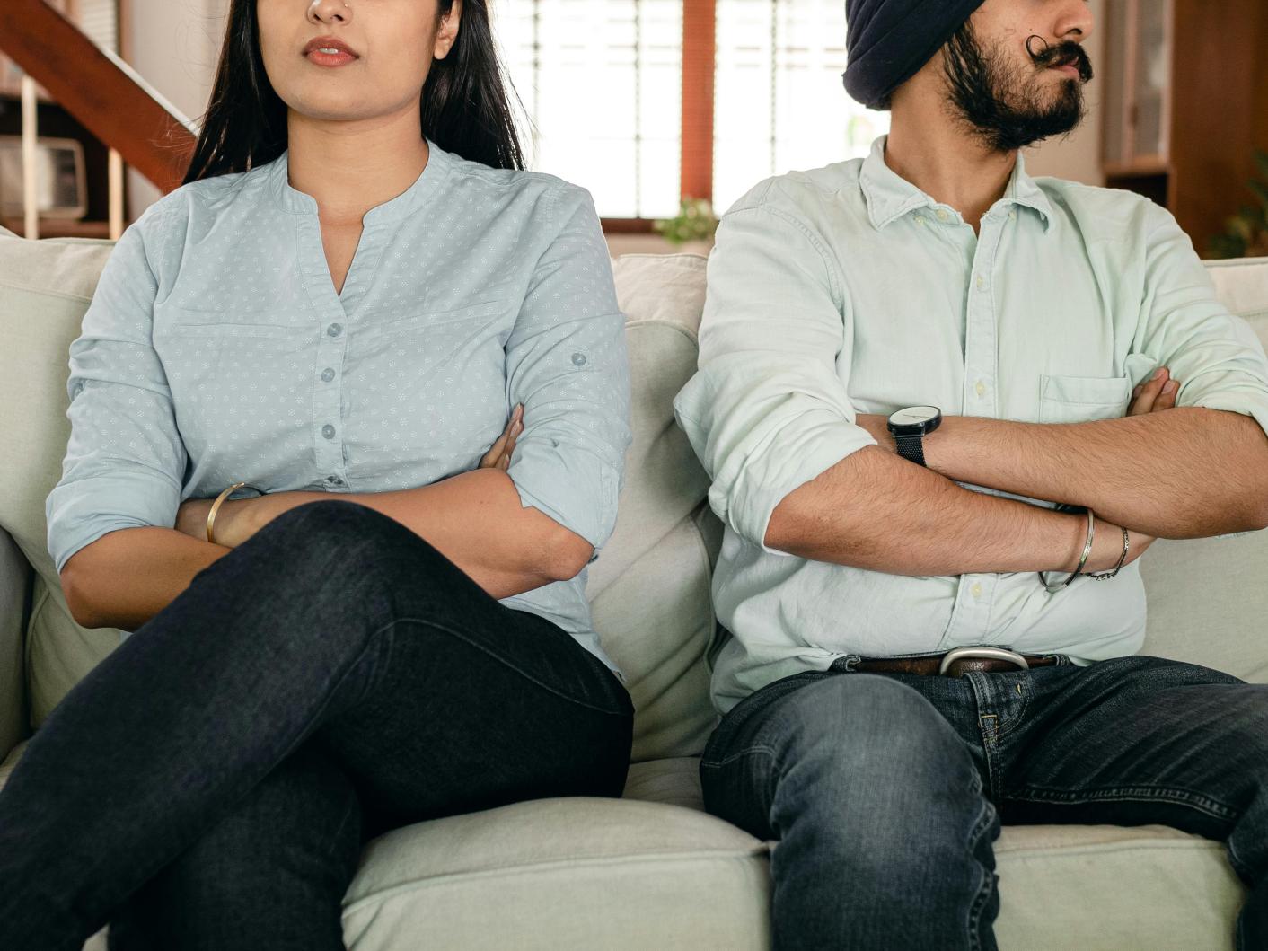 Ethnic couple sitting on sofa having marriage issues